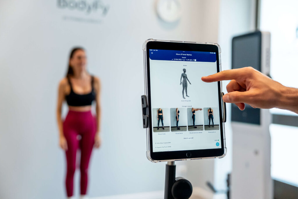 Una persona utilizza la valutazione digitale del fitness di Bodyfy su un tablet, mentre una donna sta dietro.