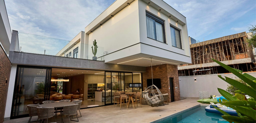 Moderna casa a due piani con patio, zona pranzo all’aperto, piscina e ampie finestre.